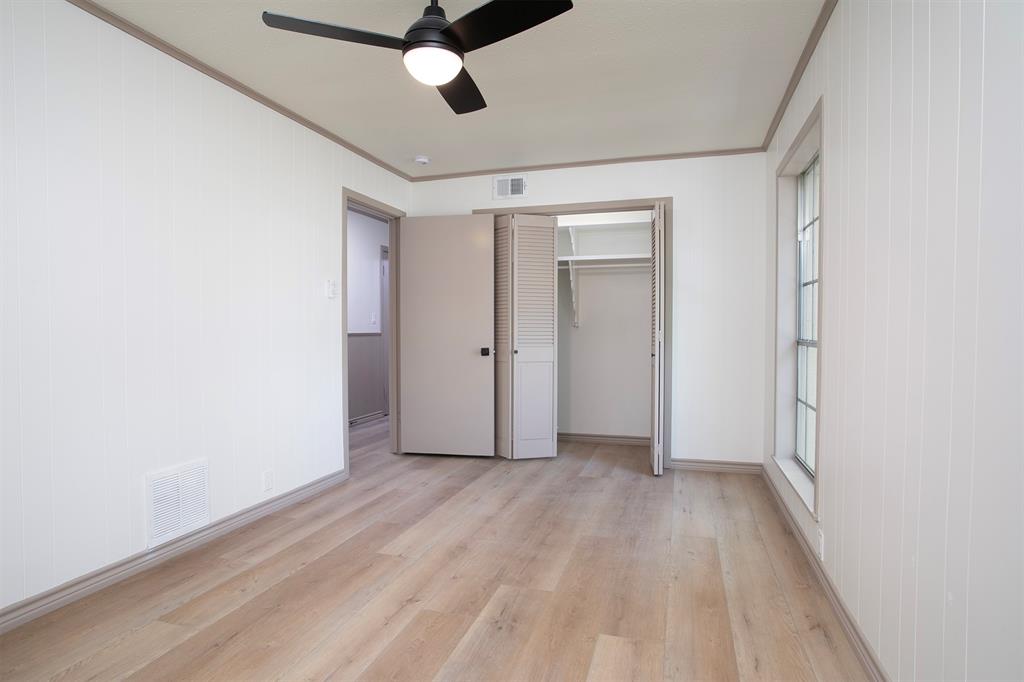 Room featuring vertical wall paneling, wood-finish flooring, a ceiling fan with integrated lighting, and a closet with bifold louvered doors