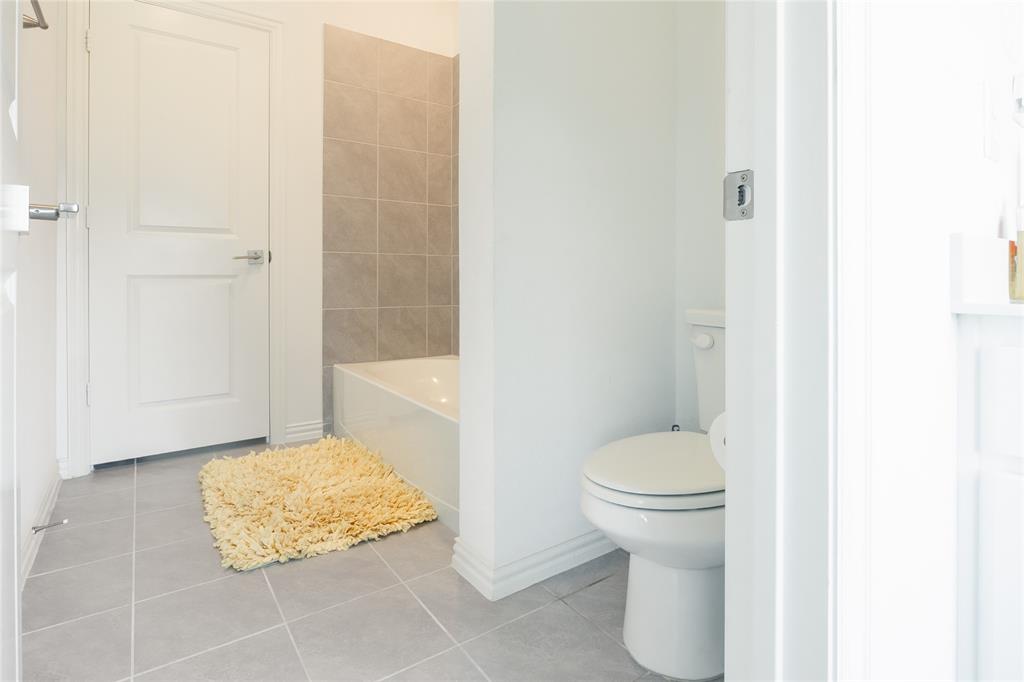Bathroom featuring grey tile flooring, a bathtub with neutral wall tile surround, and a white toilet