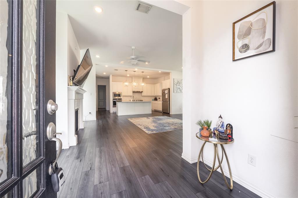 Entryway featuring a dark-framed glass-panel door, wood-finish flooring, and a fireplace with a decorative mantel, extending toward a kitchen with white cabinetry and a center island