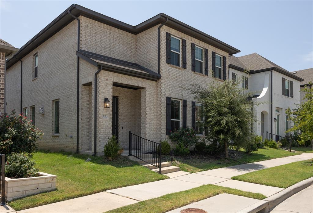Light brick exterior featuring dark-toned window shutters, a covered entry with metal handrails, and low-maintenance landscaping
