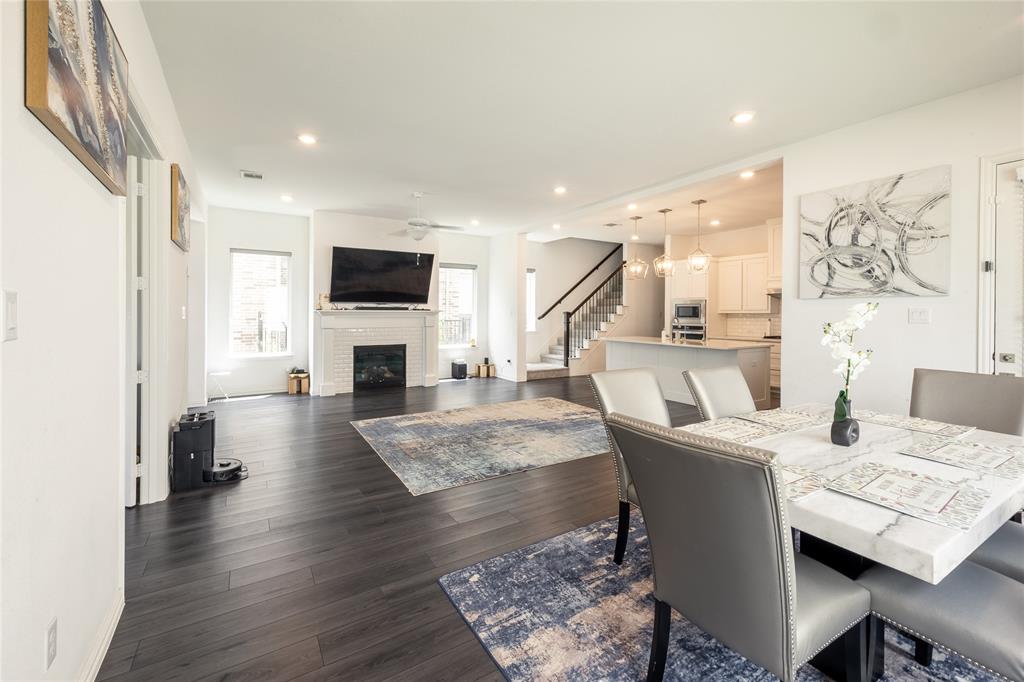 Open-concept interior featuring wood-finish flooring, a white brick-surround fireplace, recessed lighting, and a kitchen island with pendant fixtures