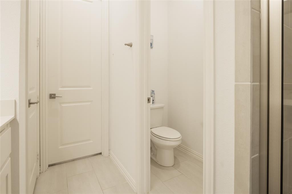 Neutral-toned ceramic tile flooring, solid-core paneled interior door with a satin nickel lever handle, and a standard-profile elongated toilet