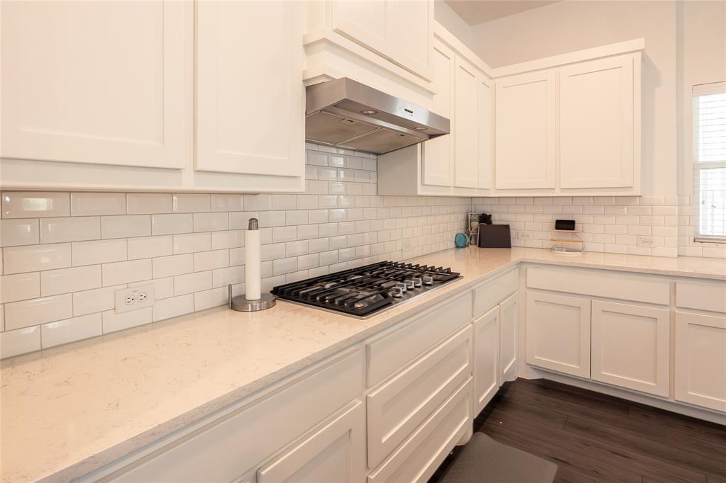 Kitchen featuring shaker-style cabinetry, subway tile backsplash, light-toned stone-finish countertops, stainless steel gas cooktop, and stainless steel range hood