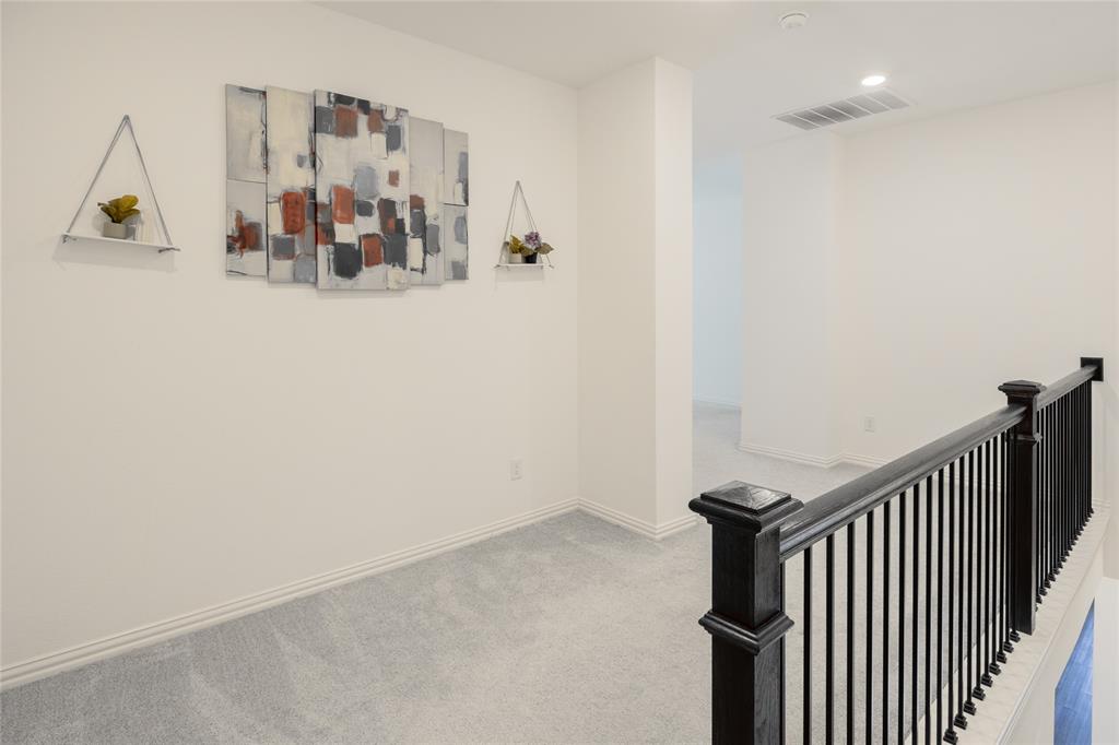Neutral-toned carpeted hallway featuring recessed ceiling lighting, a dark wood railing with black metal spindles, and white walls