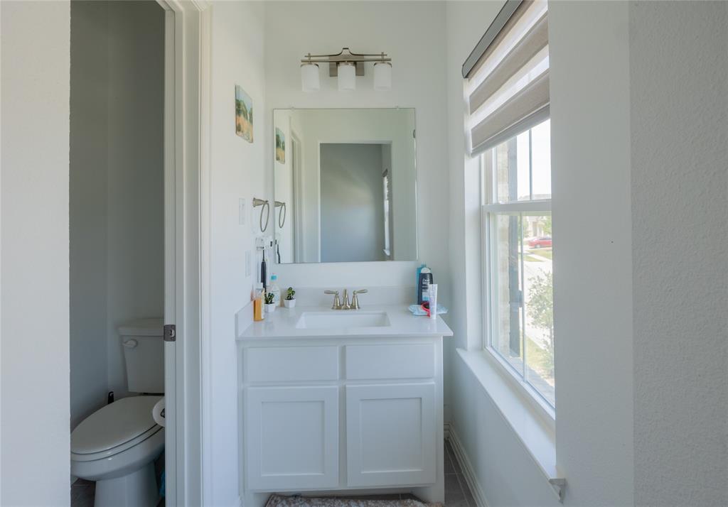 Bathroom vanity featuring a white cabinet, stone-finish countertop, undermount sink, and polished metal widespread faucet, accented by a three-light vanity fixture and frameless mirror