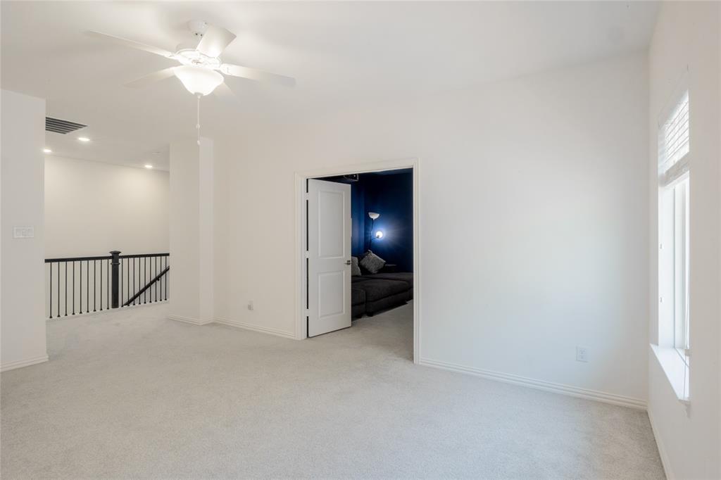 Room featuring neutral wall-to-wall carpeting, ceiling fan with integrated lighting, dual-panel interior door, and a metal baluster staircase railing