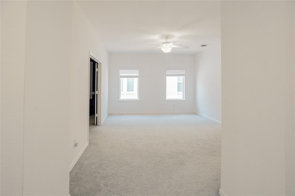 Interior space featuring neutral wall-to-wall carpeting, dual windows with roller shades, and a ceiling-mounted light fixture with fan blades