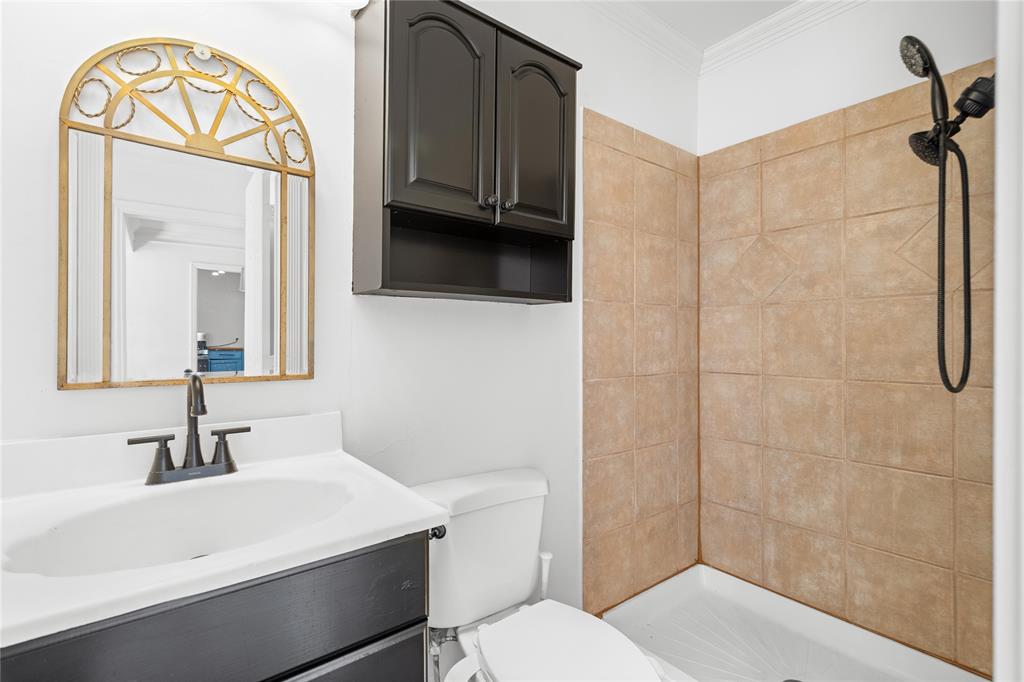Bathroom featuring a vanity with dark cabinetry, integrated countertop, and matte black faucet, wall-mounted dark storage cabinet, and tiled shower enclosure with a handheld shower head