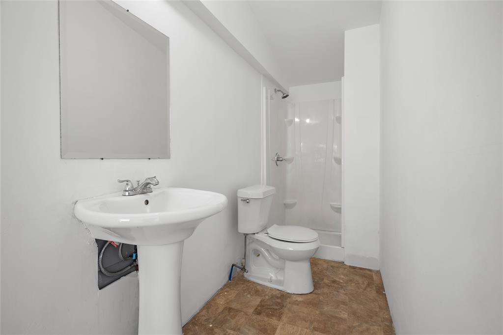 Pedestal sink with chrome faucet, wall-mounted mirror, two-piece toilet, and shower enclosure with integrated shelving