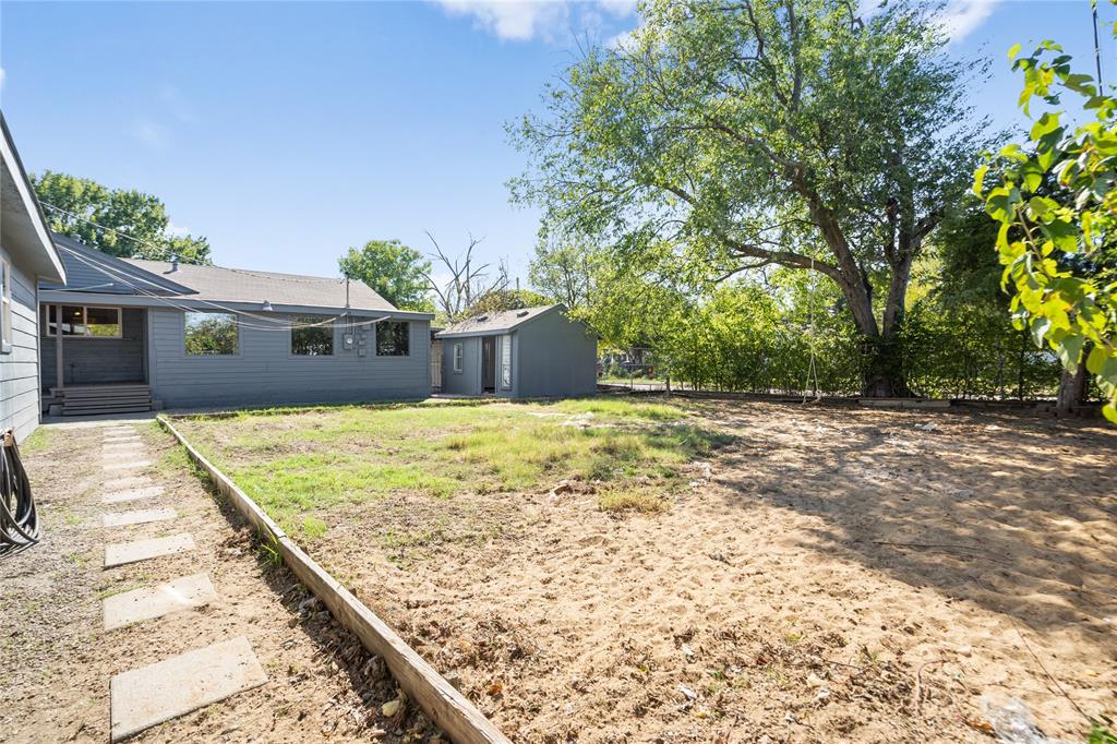 Spacious backyard featuring a detached structure, concrete paver path, mature trees, and perimeter fencing