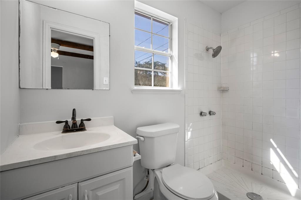 Bathroom featuring a vanity with an integrated sink and bronze-finish faucet, a wall-mounted frameless mirror, a single-hung window, and a tiled shower enclosure