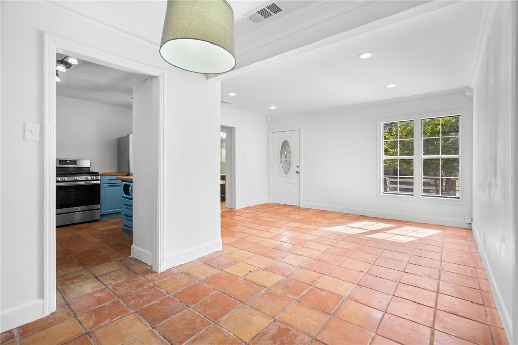 Open interior space featuring terra-cotta tile flooring, recessed lighting, crown molding, and an exterior door with decorative oval glass inlay