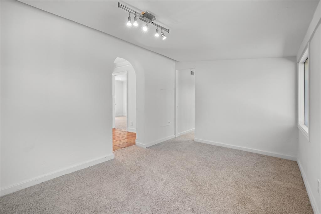 Interior space featuring neutral wall-to-wall carpeting, an arched doorway, and a ceiling-mounted four-light track fixture
