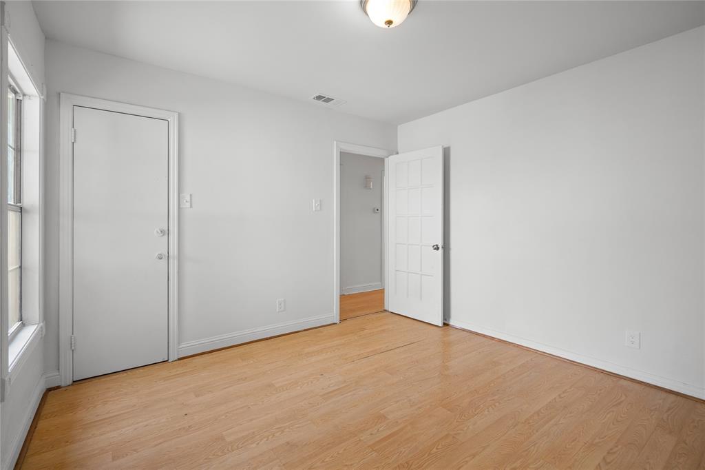 Room featuring wood-finish flooring, white walls, flush-mount ceiling lighting, a solid-panel door, and a multi-pane glass door