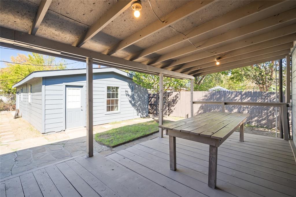 Covered deck with painted wood decking, overhead support beams, and exposed rafters, featuring an integrated flagstone patio and a detached structure with horizontal siding