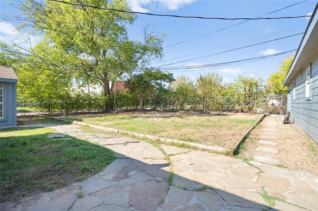 Backyard space featuring stone hardscaping, a raised garden bed with timber edging, chain-link perimeter fencing, and mature trees