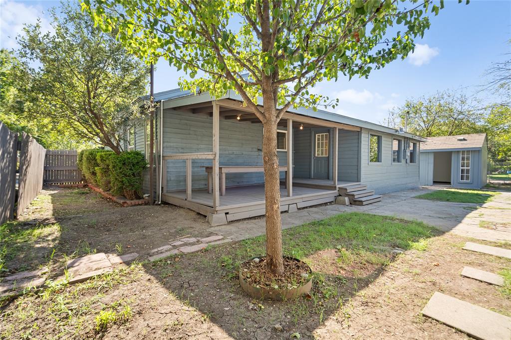 Exterior backyard space featuring a covered wooden deck, detached storage structure, privacy fencing, and mature trees