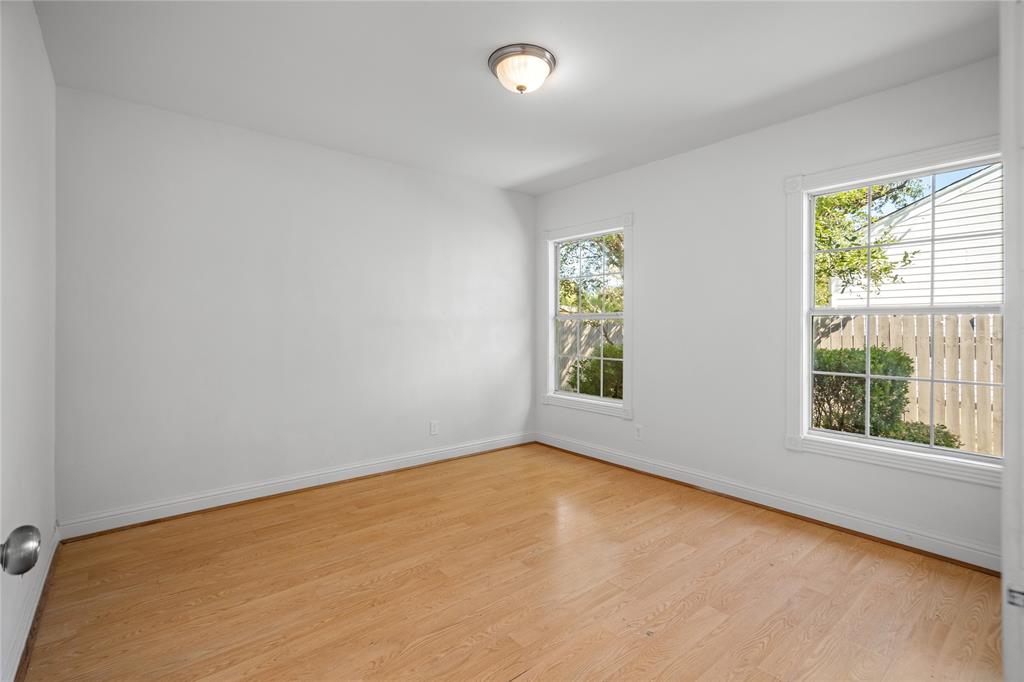 Neutral-toned room featuring wood-finish flooring, two dual-pane windows with muntins, and a central flush-mount ceiling light fixture