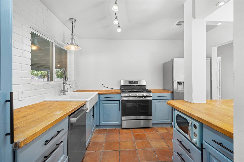 Kitchen featuring blue cabinetry, wood countertops, a white apron-front sink, stainless steel appliances, and terracotta tile flooring
