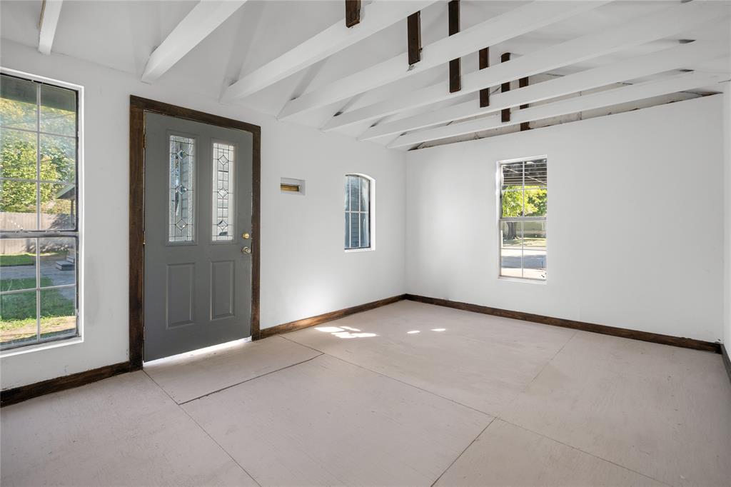 Interior space featuring exposed white-painted rafters, multiple windows with grid detailing, and an exterior door with decorative glass panes