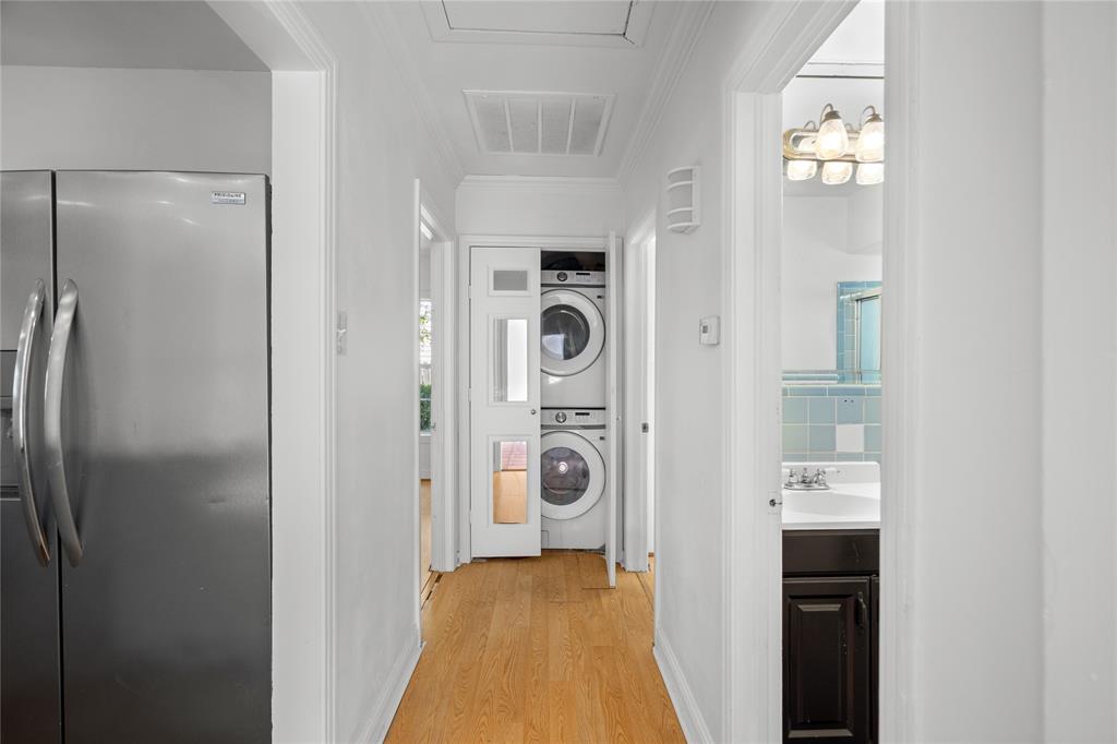Stainless steel refrigerator, wood-finish flooring, stackable washer and dryer, glass-paneled closet door, and vanity with dark-finish cabinetry