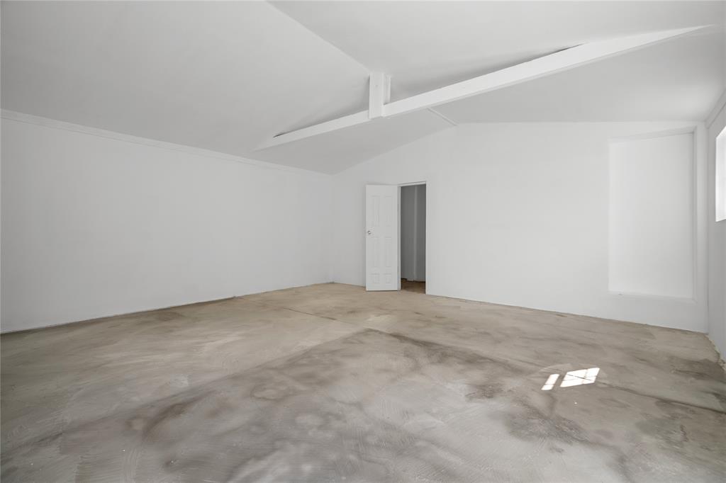 Interior space featuring vaulted ceilings, a structural support beam, concrete flooring, and a six-panel interior door