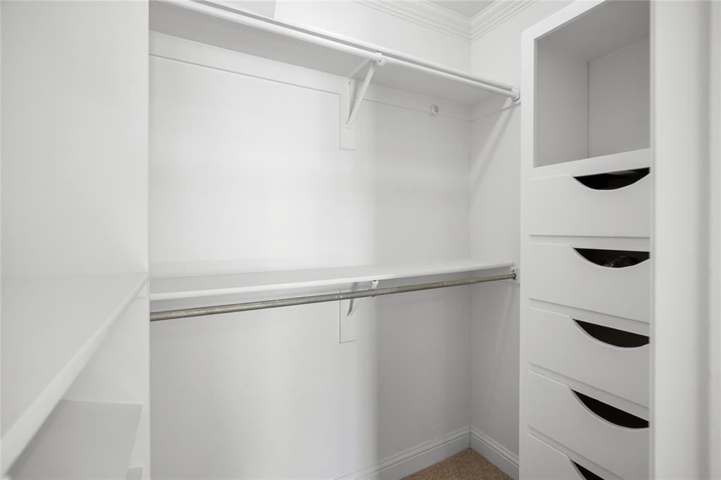 Walk-in storage space featuring built-in white cabinetry, integrated drawers with recessed pulls, tiered shelving, and metal hanging rods