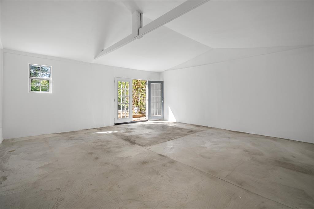 Vaulted ceilings with exposed structural beam, concrete flooring, and French door entry