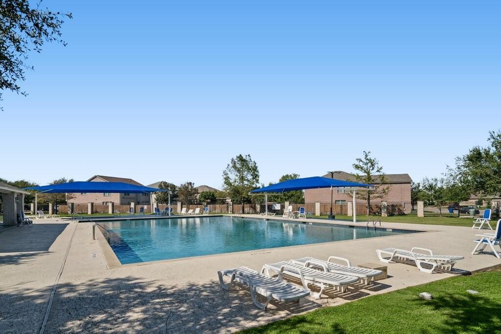 In-ground swimming pool featuring concrete decking, dual blue fabric shade structures, and perimeter fencing