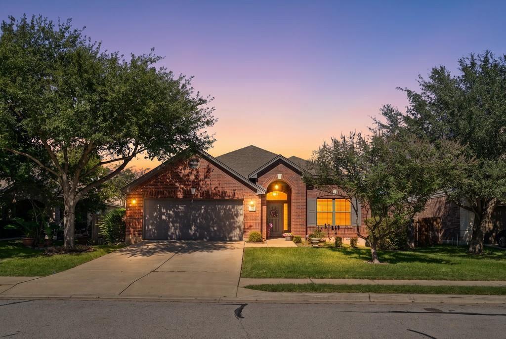 Brick exterior featuring an arched entryway, shingle roofing, concrete driveway, and mature landscaping Brick exterior featuring an arched entryway, shingle roofing, concrete driveway, and mature landscaping