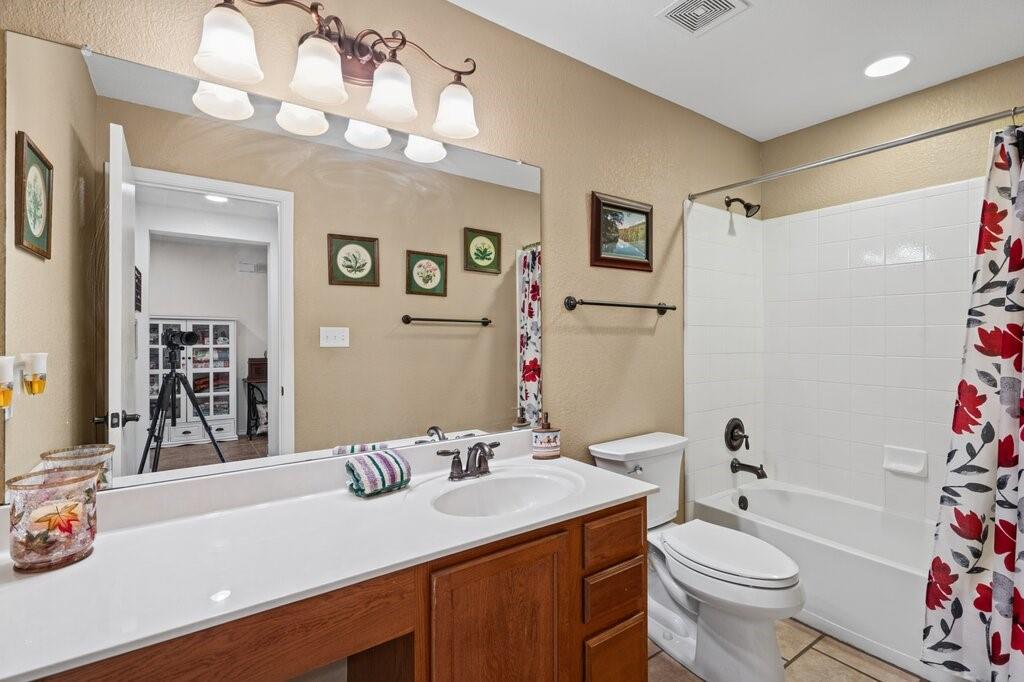 Bathroom featuring wood-finish cabinetry, white solid-surface countertop with an integrated oval sink, full-width wall mirror, multi-light vanity fixture, and a tub-shower combination with white tile surround