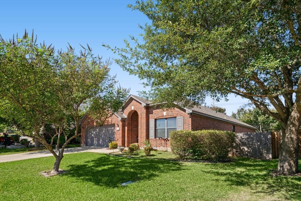 Single-story brick exterior featuring an arched entryway, shingled roof, attached garage, and mature landscaping Single-story brick exterior featuring an arched entryway, shingled roof, attached garage, and mature landscaping