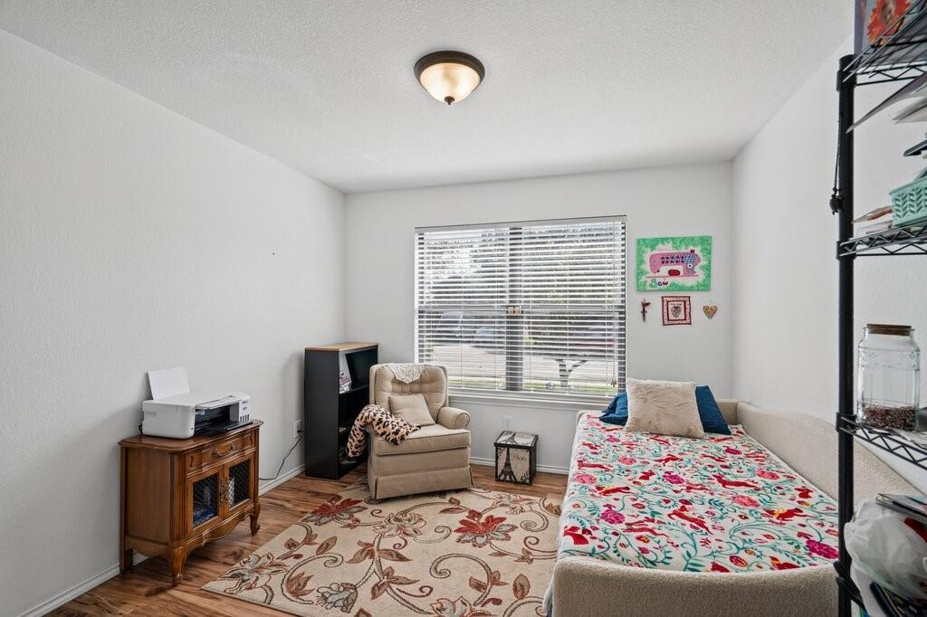 Wood-finish flooring, neutral walls, large window with horizontal blinds, and a dome-style flush-mount ceiling light fixture