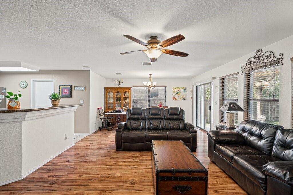 Open-concept interior featuring wood-finish flooring, a central ceiling fan with integrated lighting, a raised kitchen counter, and sliding glass doors Open-concept interior featuring wood-finish flooring, a central ceiling fan with integrated lighting, a raised kitchen counter, and sliding glass doors