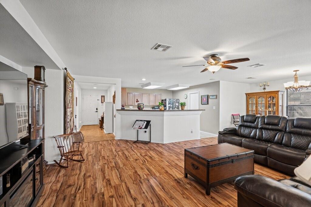 Living area featuring wood-finish flooring, recessed ceiling lighting, a multi-blade ceiling fan with integrated light fixture, and a peninsula counter Living area featuring wood-finish flooring, recessed ceiling lighting, a multi-blade ceiling fan with integrated light fixture, and a peninsula counter