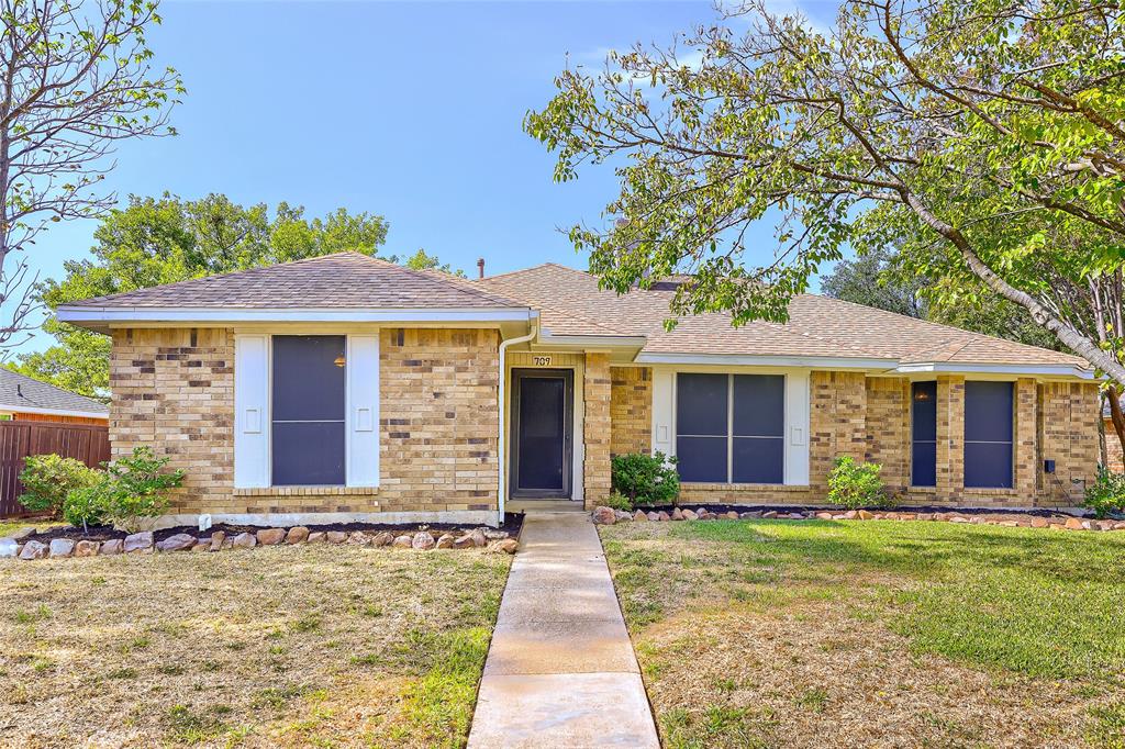 Single-story brick exterior featuring a multi-gable roofline, stone-lined garden beds, and a concrete front walkway Single-story brick exterior featuring a multi-gable roofline, stone-lined garden beds, and a concrete front walkway