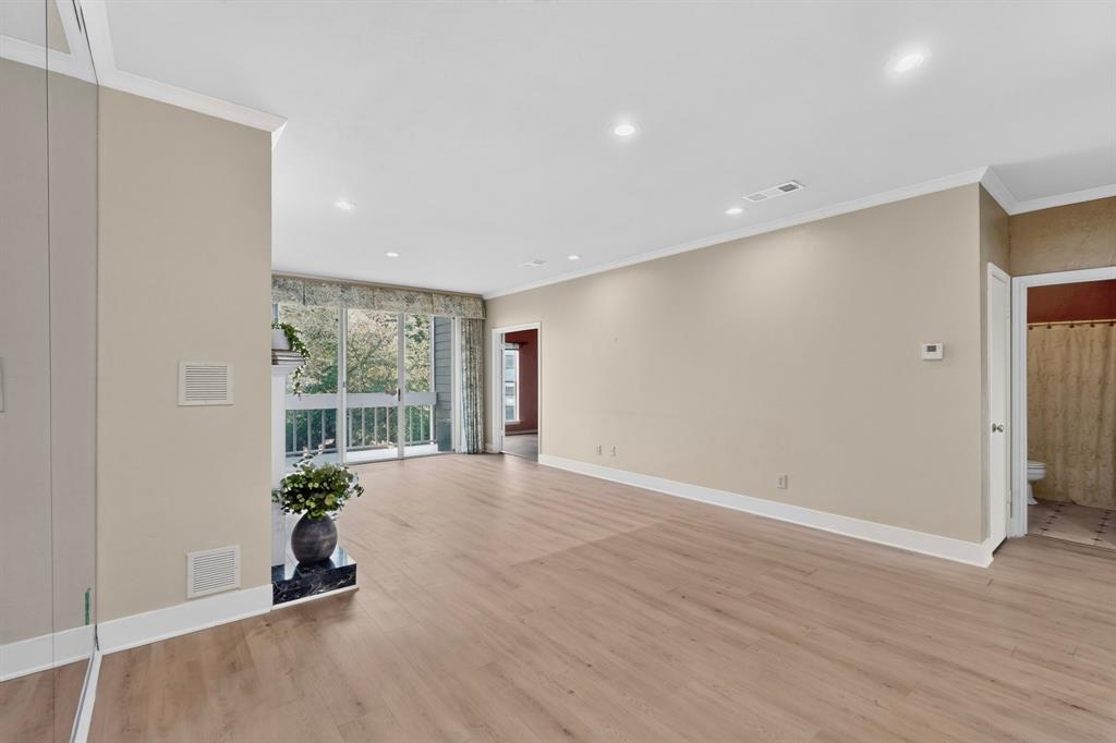 Open-concept interior featuring light wood-finish laminate flooring, recessed lighting, crown molding, a sliding glass door with a balcony, and a fireplace with a raised hearth.