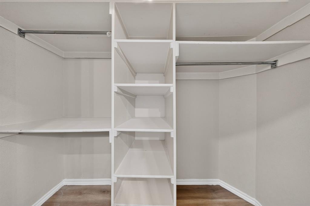 Wrapped within the primary ensuite bathroom is this walk-in closet featuring built-in shelving, dual clothing rods, and newly installed wood-finish laminate flooring.