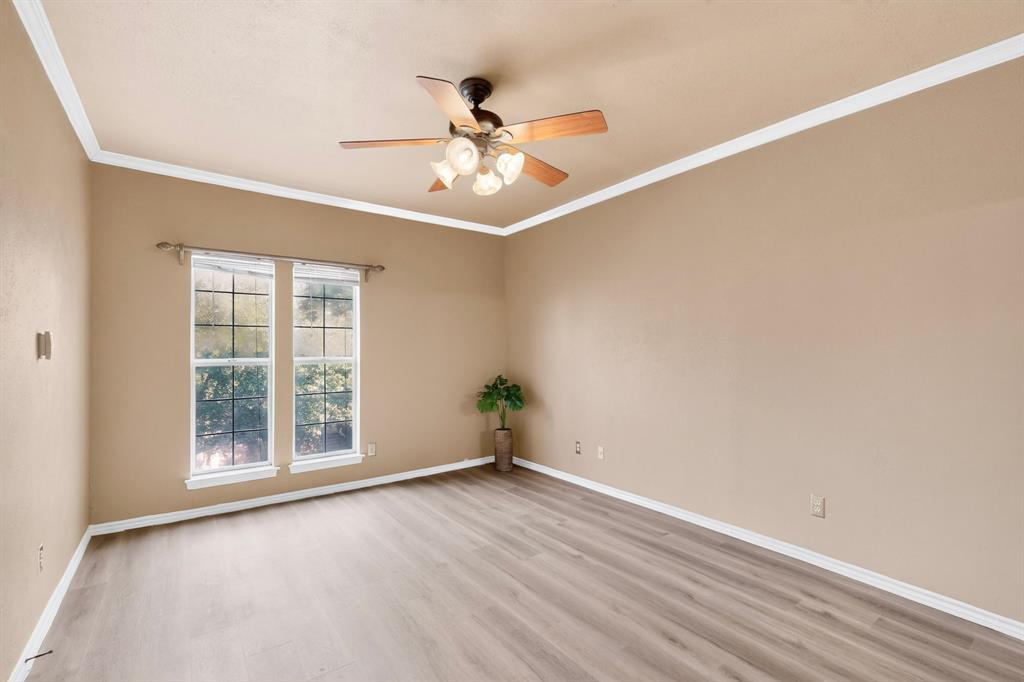 Primary bedroom featuring newly installed wood-finish laminate flooring, crown molding, and a ceiling fan with integrated light fixture.