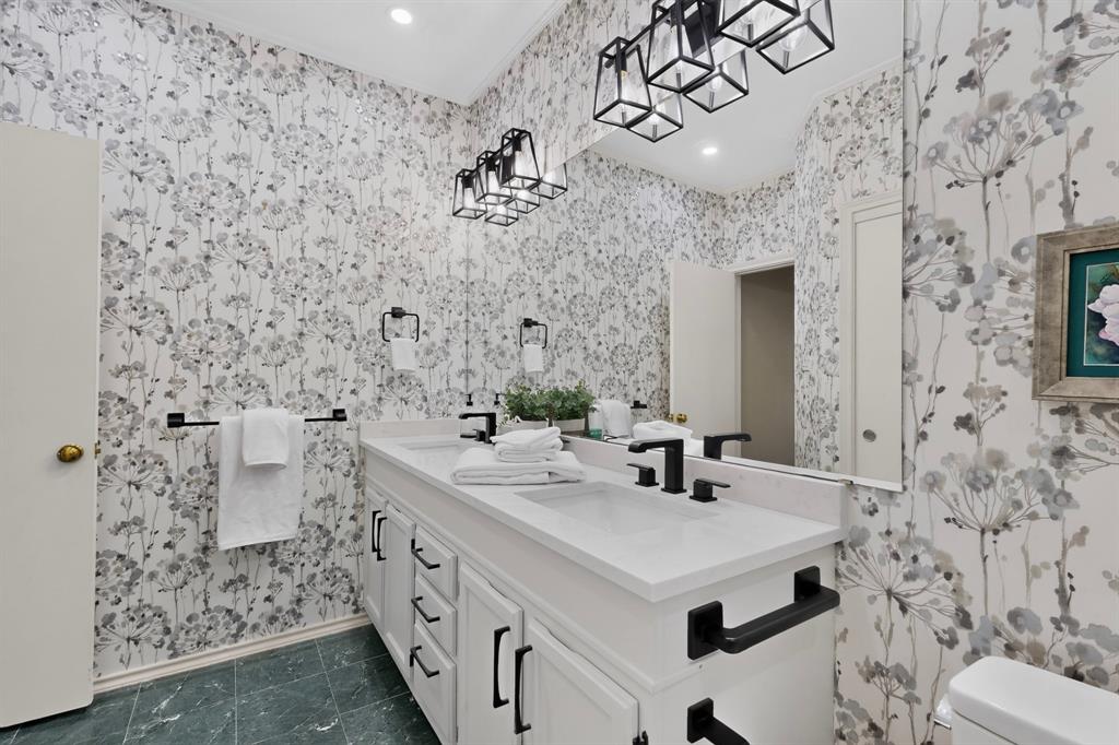 Double vanity with white cabinetry, stone-finish countertops, and matte black hardware create a modern finish in this updated ensuite primary bathroom.