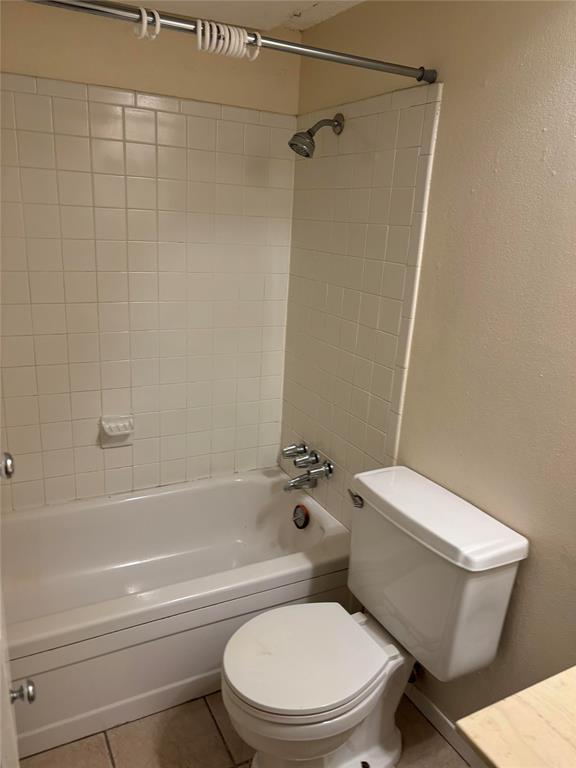 Bathroom with tile floors, toilet, and tiled shower / bath combo