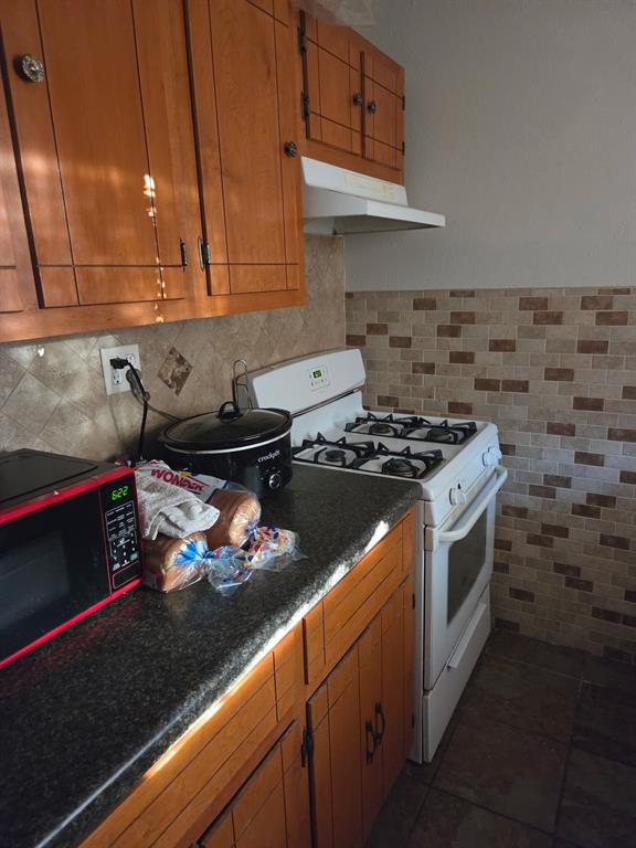 Kitchen featuring stained wood cabinetry, stone-texture countertops, a tiled backsplash, and an integrated range hood Kitchen featuring stained wood cabinetry, stone-texture countertops, a tiled backsplash, and an integrated range hood