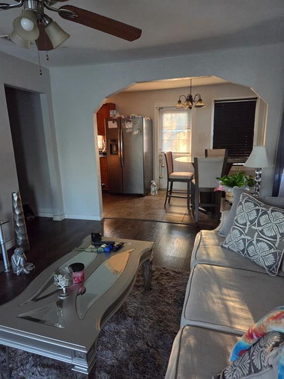 Interior featuring wood-finish flooring, a decorative arched wall opening, a stainless-steel refrigerator, tile flooring, and a ceiling fan with integrated lighting Interior featuring wood-finish flooring, a decorative arched wall opening, a stainless-steel refrigerator, tile flooring, and a ceiling fan with integrated lighting