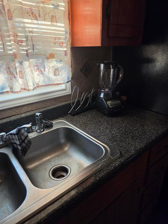 Kitchen featuring a dual-basin stainless steel sink, stone-finish countertops, tiled backsplash, and wood-finish cabinetry Kitchen featuring a dual-basin stainless steel sink, stone-finish countertops, tiled backsplash, and wood-finish cabinetry
