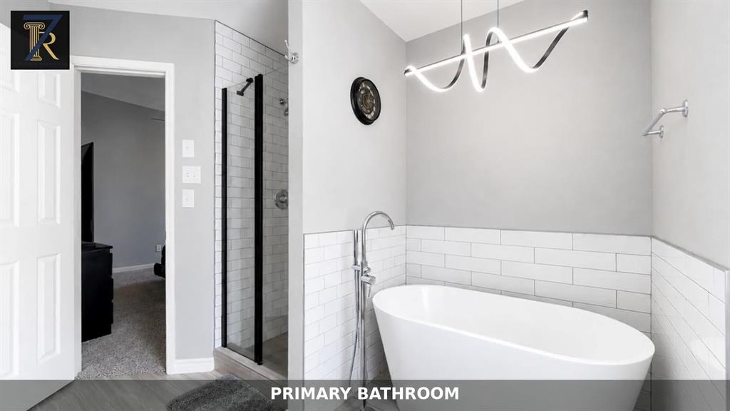 Freestanding soaking tub with a chrome floor-mounted faucet, walk-in shower with black-framed glass enclosure, and white subway tile surrounds