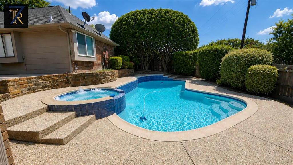 Custom-shaped swimming pool featuring a built-in spa, aggregate concrete decking, stone masonry retaining walls, and tiered entry steps