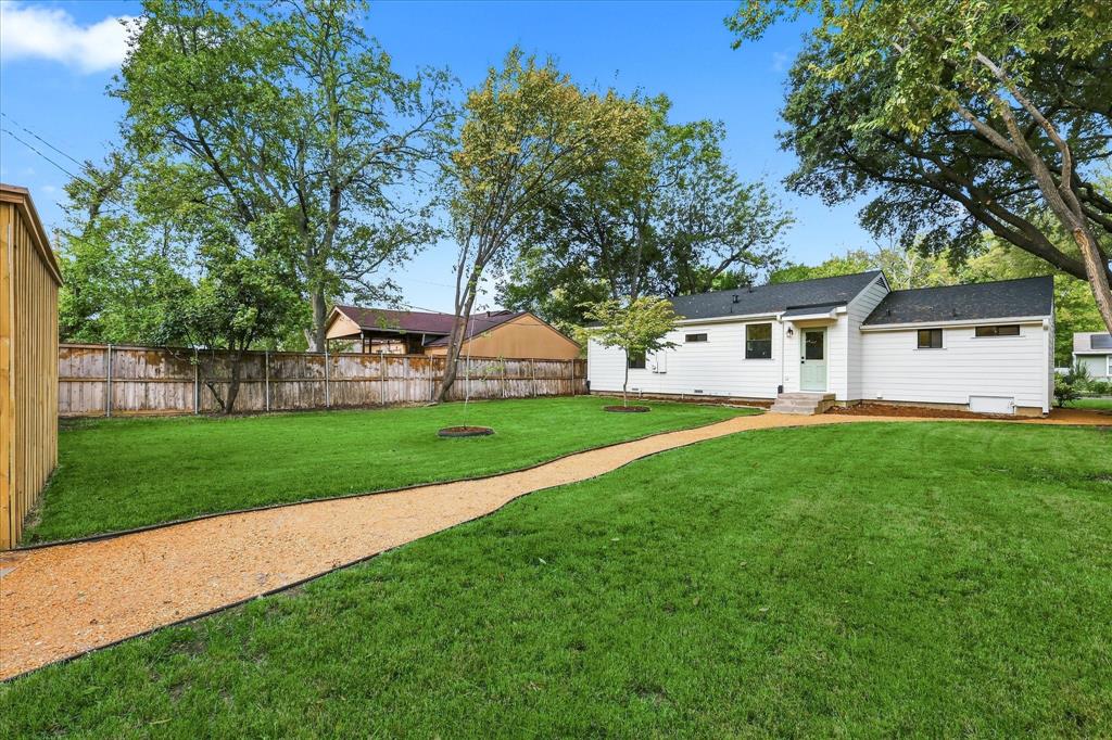 Expansive backyard featuring a manicured lawn, gravel pathway, wood privacy fencing, and mature trees