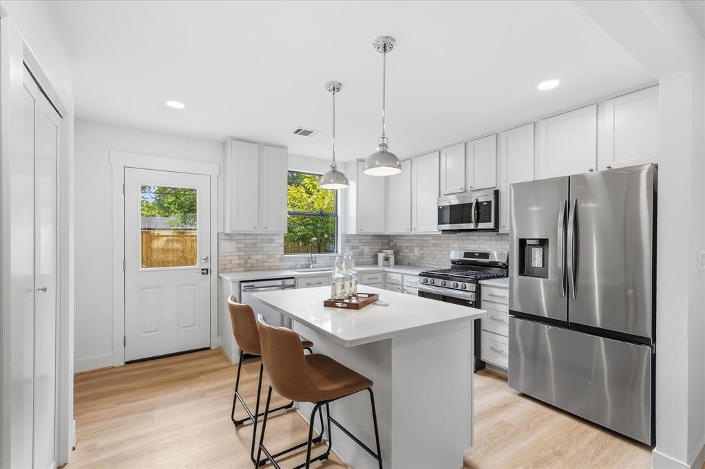 Kitchen featuring white shaker-style cabinetry, quartz countertops, a central island, stainless steel appliances, and wood-finish flooring
