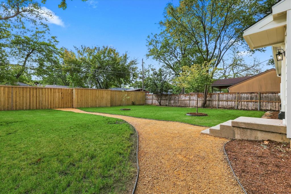 Private backyard featuring a manicured lawn, gravel pathway, wood privacy fencing, and concrete steps