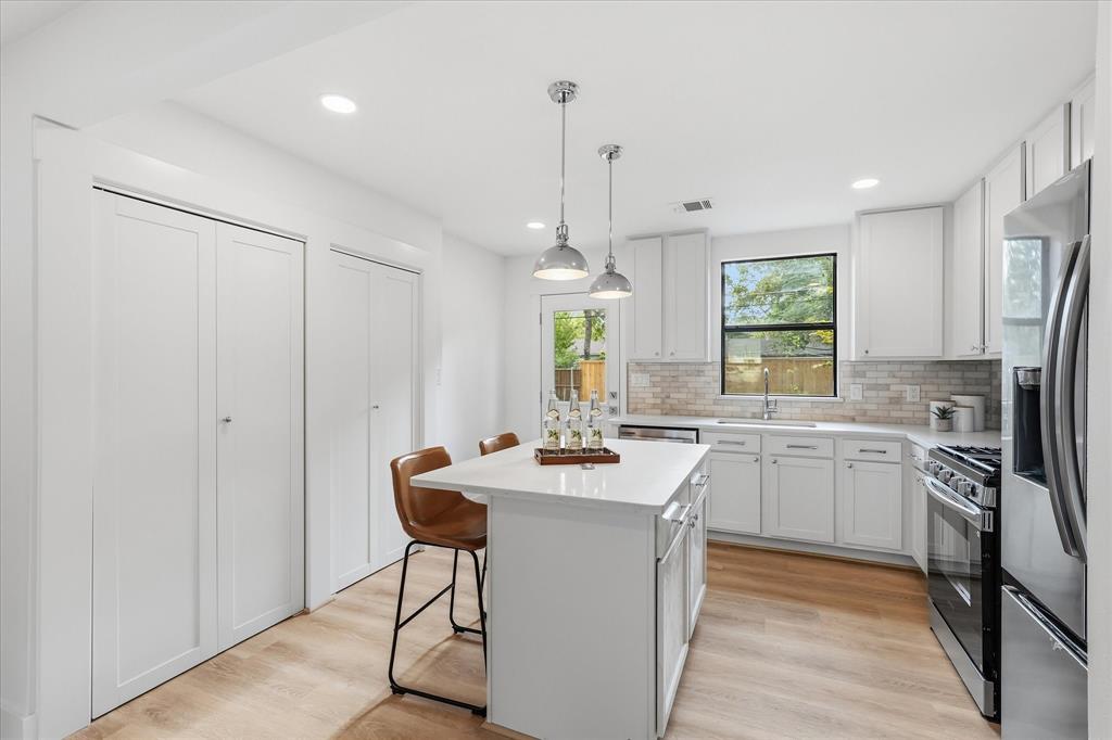 Kitchen featuring white shaker-style cabinetry, a central island with a solid-surface countertop, subway tile backsplash, stainless steel appliances, and wood-finish flooring